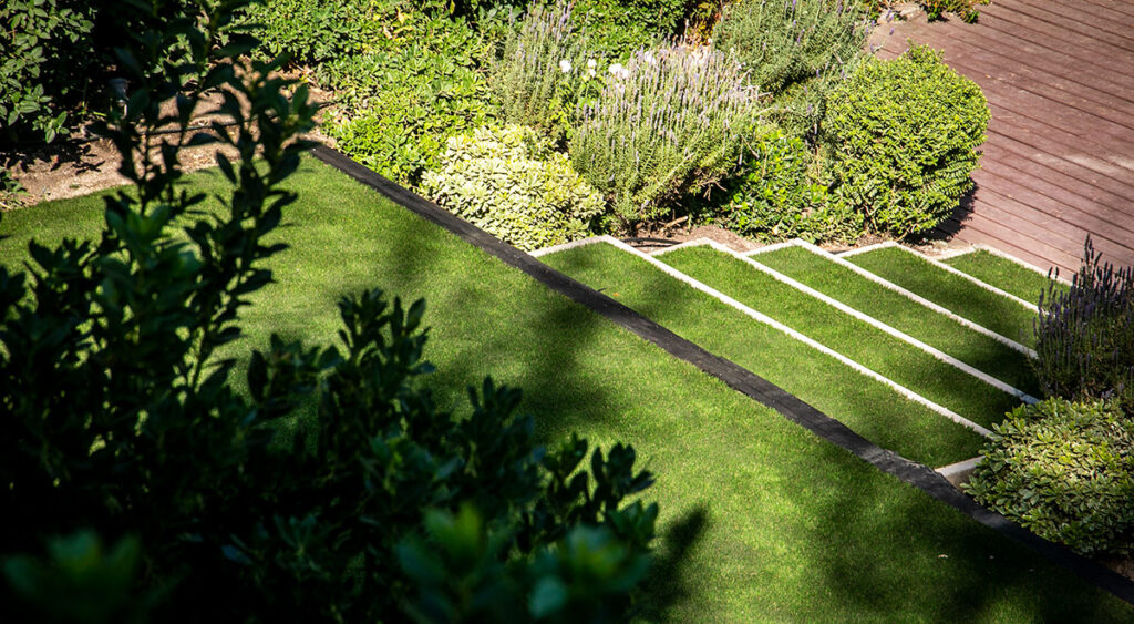 Jardín con pasto sintético y vegetación natural. 