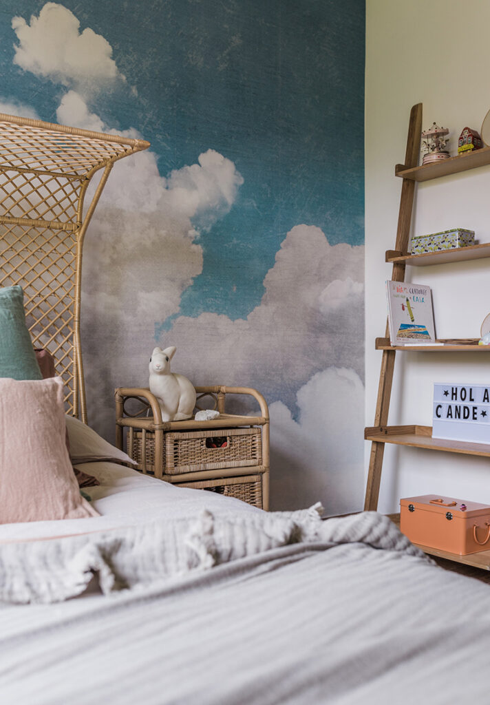 Dormitorio infantil con papel mural de nubes y muebles de mimbre y madera.